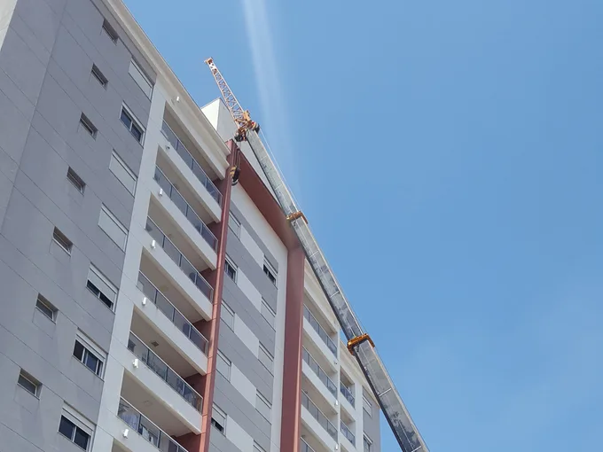 Guindaste Pega Peso operando ao lado de um prédio residencial de múltiplos andares em Piracicaba